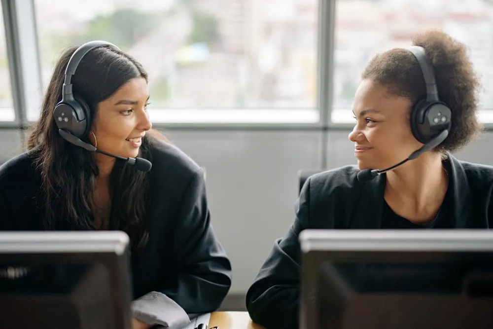 Two customer service agents wearing headsets smiling at each other at their desks